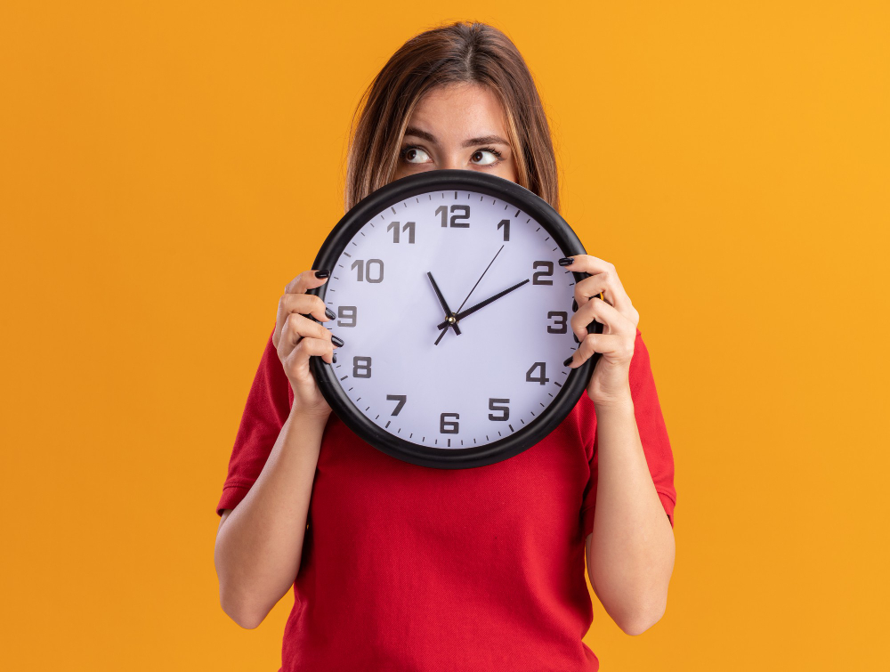 /upl/confused-young-pretty-woman-holds-clock-looking-at-side-isolated-on-orange-wall.jpg